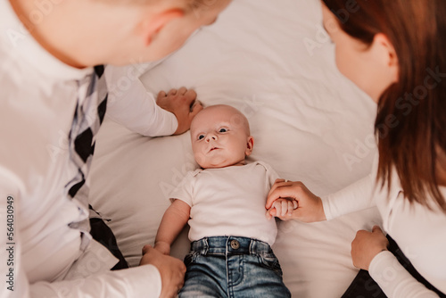 Little boy cute child baby playing with parents. Toddler lying on bed having fun dressed blue jeans and white t-shirt. Happy childhood, family concept 
