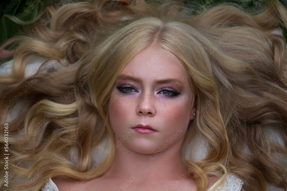 Naklejka premium Close-up portrait of beautiful preteen girl with curly blond hair and facial frecles lying on her back. Serene people. Selective focus. Beauty and Fashion theme.