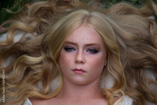 Close-up portrait of beautiful preteen girl with curly blond hair and facial frecles lying on her back. Serene people. Selective focus. Beauty and Fashion theme.