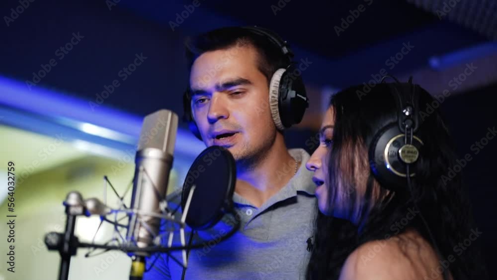 Couple recording a song in the studio. Duet singing emotionally in front of professional microphones. Couple recording a song in the studio. Duet singing emotionally in front of professional microphones.