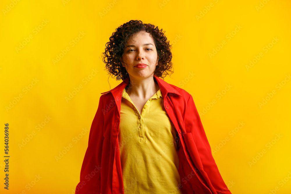 Curly cute girl smiling and jumping. Studio portrait of a pretty young caucasian woman on a bright yellow background. Positive active female in bright clothes. Copy space.