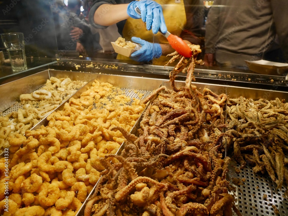 Obraz premium Woman behind counter at Mercado de San Miguel putting mixed fried seafood in bags. Madrid, Spain.
