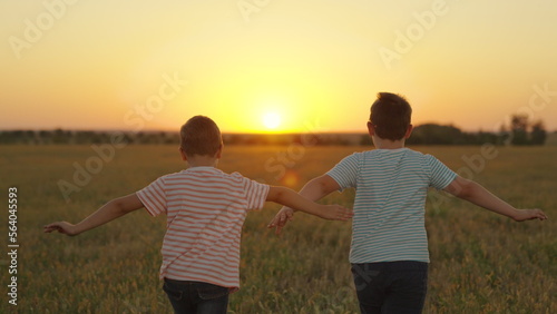 Kids play superheroes, nature. Boys friends, aviators run with their hands raised like an airplane across field in rays of sunset. Children want to become an astronaut. Teenager dreams of flying