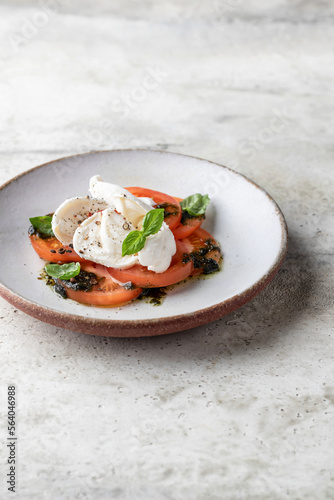Caprese salad in modern feed with tomatoes, basil, mozzarella, pesto. Traditional Italian food on gray textured background isolated with text space, menu