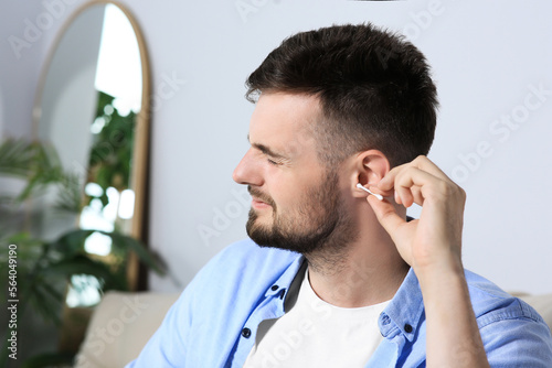 Young man cleaning ear with cotton swab at home. Space for text