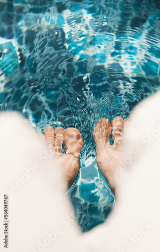 Person sitting on the edge of swimming pool and putting legs into the water