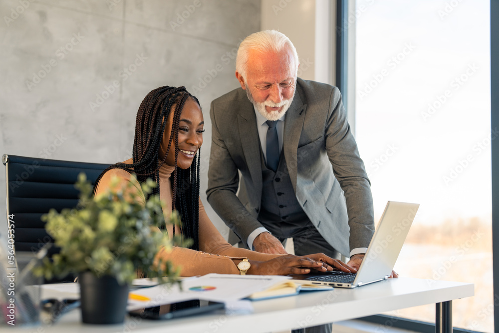 Φωτογραφία Young African American businesswoman leader, professional company manager using laptop, working with older European colleague, typing writing new business strategy plan