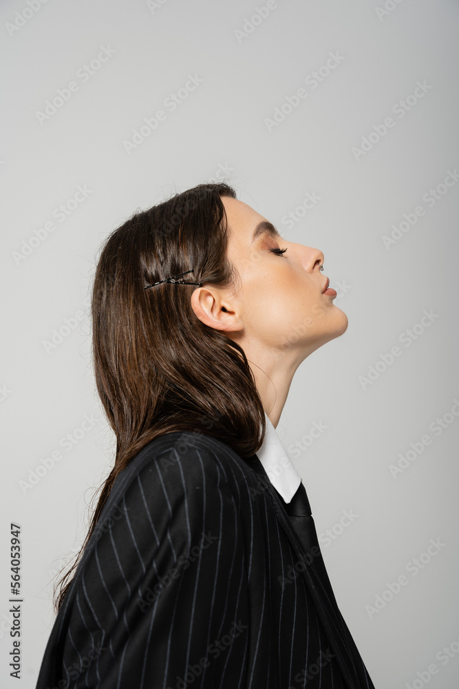 Φωτογραφία side view of young brunette woman in black and striped blazer isolated on grey
