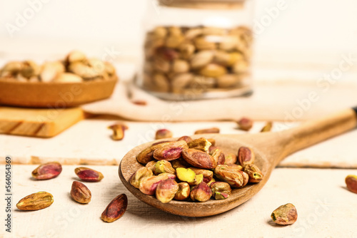 Spoon with tasty pistachio kernels on white wooden table, closeup