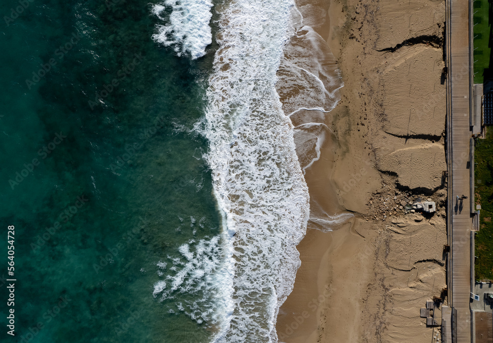 Aerial view of ocean waves breaking on a sandy beach. Beach erosion after coastal flooding. Aerial view of ocean waves breaking on a sandy beach. Beach erosion after coastal flooding.