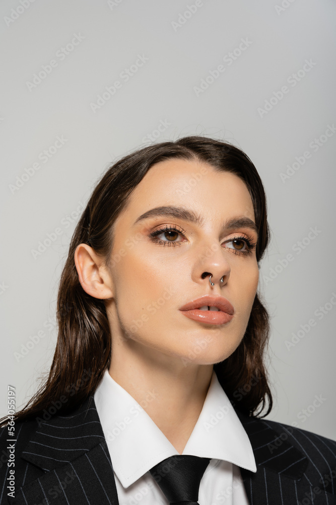 portrait of brunette woman with makeup and piercing posing in black blazer and tie isolated on grey. portrait of brunette woman with makeup and piercing posing in black blazer and tie isolated on grey.