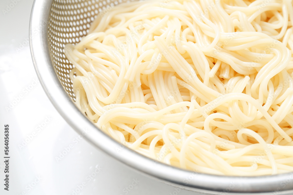 Colander with boiled pasta on light background, closeup