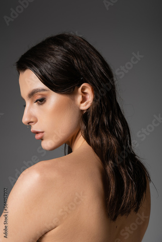 profile of sensual shirtless woman with brunette hair posing isolated on grey.