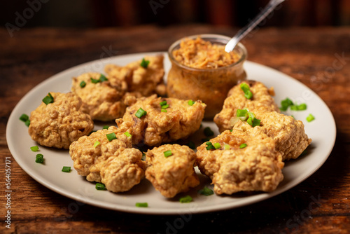 Cauliflower wings food. Pieces of cauliflower cooked in batter on a plate on a wooden background. Sprinkled with green onions.