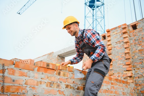 Installing brick wall. Construction worker in uniform and safety equipment have job on building