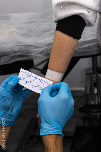 Tattoo artist measuring the drawing on the client's hand, Male tattoo artist placing a paper art on the body.