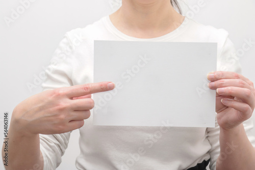 a woman holding a blank blank white sheet of paper, points with her index finger. © Marina Gordejeva