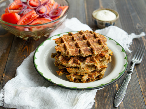Delicious eggplant wafflese in retro metal plate with tomato and onion salad and sauce ion wood background. Healthy vegeterian food. Close up, copy space.