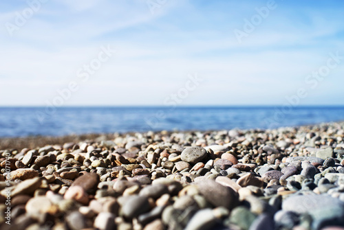 Marine background. Pebble beach on a sunny day. Pebbles close-up, sea and sky in summer without people, soft selective focus