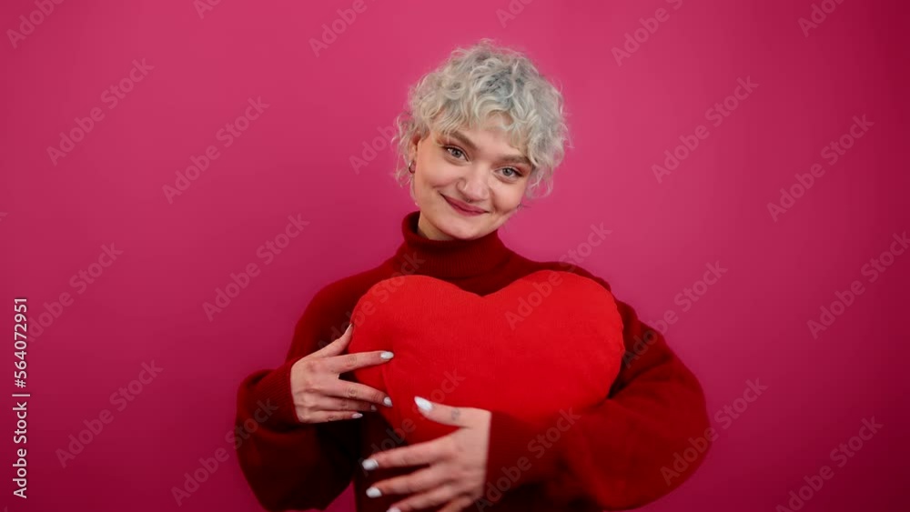 Portrait of a smiling girl looking stylish and glamorous. Close-up view of caucasian woman holding heart-shaped cushion. High quality 4k footage Portrait of a smiling girl looking stylish and glamorous. Close-up view of caucasian woman holding heart-shaped cushion. High quality 4k footage