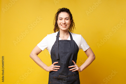 Tableau sur toile portrait of young barista girl in uniform on a yellow background, woman waiter i