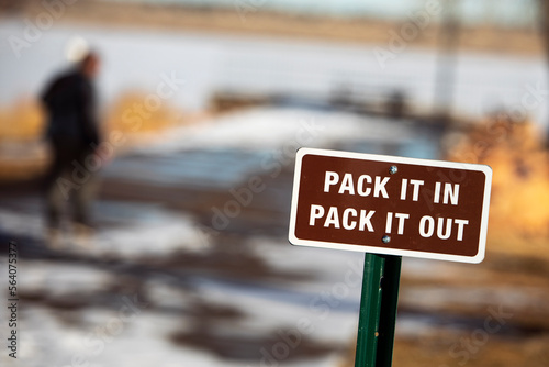 a brown, pack it in, pack it out sign with white lettering and white boarder