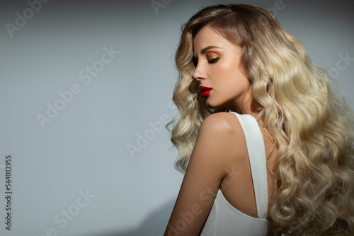 Fashion woman portrait. Beautiful curly blonde woman with long hair and bright makeup. blue background