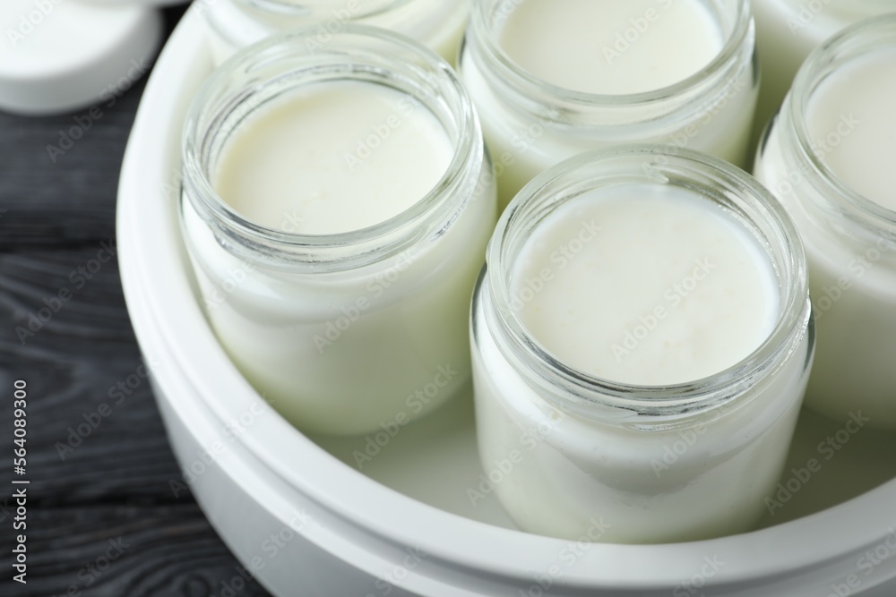 Modern yogurt maker with full jars on black wooden table, closeup Modern yogurt maker with full jars on black wooden table, closeup