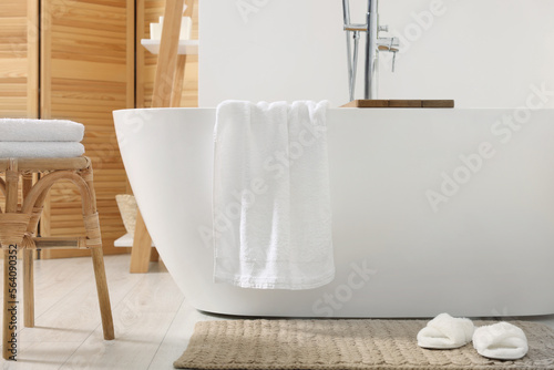 Stylish tub  wicker stool  slippers and soft towels in bathroom