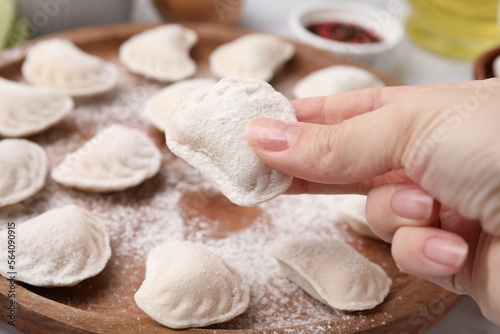 Woman holding raw dumpling (varenyk) with tasty filling at wooden board, closeup