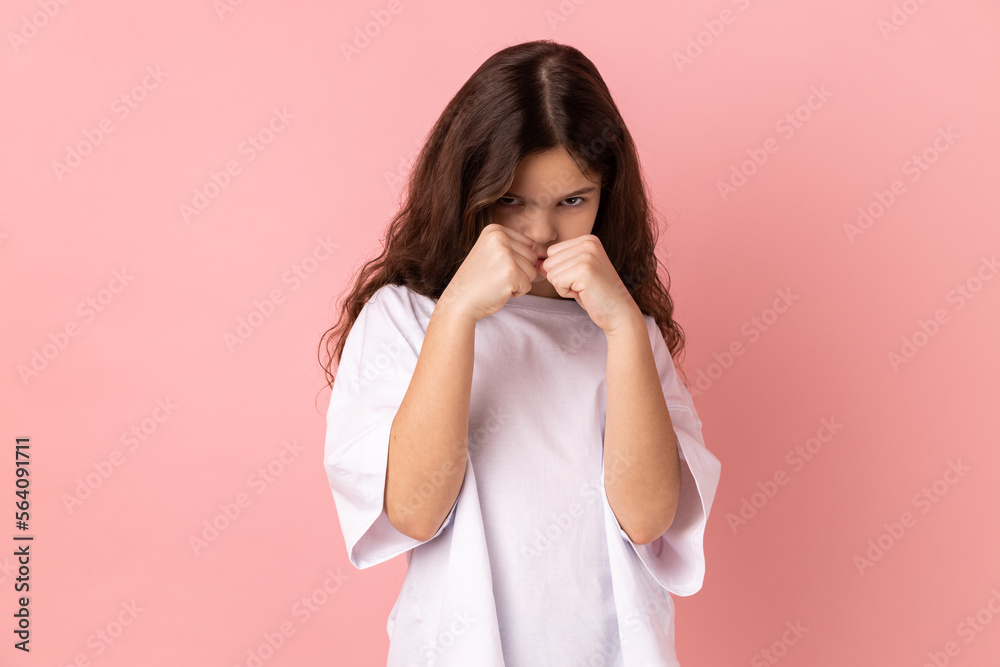 Portrait of serious concerned little girl wearing white T-shirt holding clenched fists up ready to boxing, kids self defense courses, fight spirit. Indoor studio shot isolated on pink background. Portrait of serious concerned little girl wearing white T-shirt holding clenched fists up ready to boxing, kids self defense courses, fight spirit. Indoor studio shot isolated on pink background.