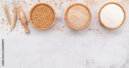  Wheat grains , brown wheat flour and white wheat flour in wooden bowl set up on white concrete background.