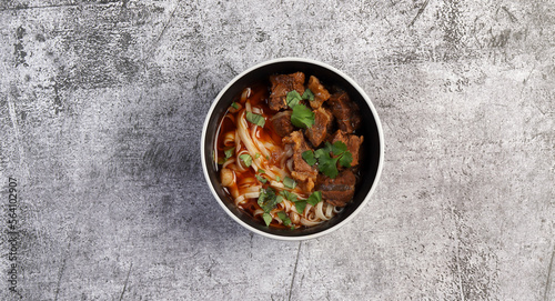 Spicy beef noodle soup or ramen with herbs in bowl on a dark gray background. Top view, flat lay