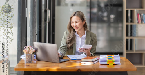 Asian Businesswoman Using laptop computer and working at office with calculator document on desk, doing planning analyzing the financial report, business plan investment, finance analysis concept.
