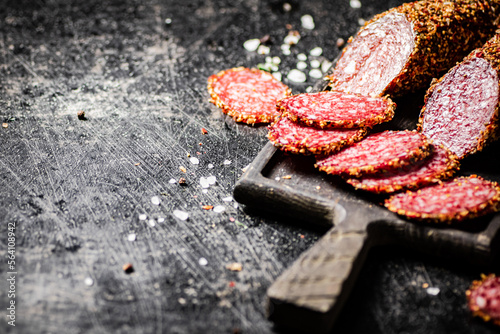 Sliced salami sausage on a cutting board with spices. 