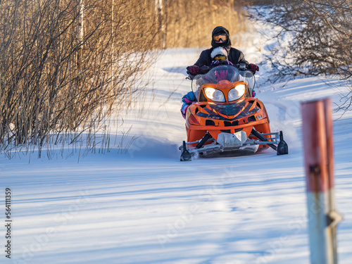 Man with child riding on a snowmobile on the snow in winter