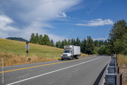 Middle rig semi truck with refrigerated box trailer driving on the highway road with hills on the sides