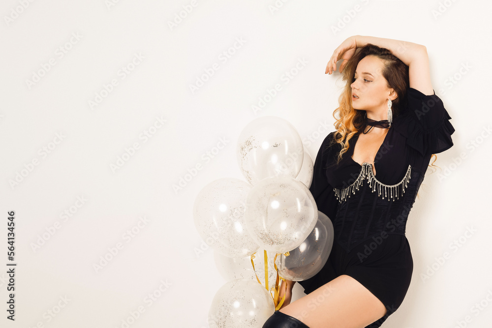 Gorgeous woman with balloons in black dress and corset with jewelry, long wavy hair posing on white background. Fashion , all black style. Gorgeous woman with balloons in black dress and corset with jewelry, long wavy hair posing on white background. Fashion , all black style.