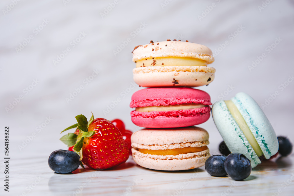 Macaron pink, orange and beige, blue on marble style. A beautiful and beautiful French dessert. Fruits, Strawberries and lingonberries, blueberries, raspberries.