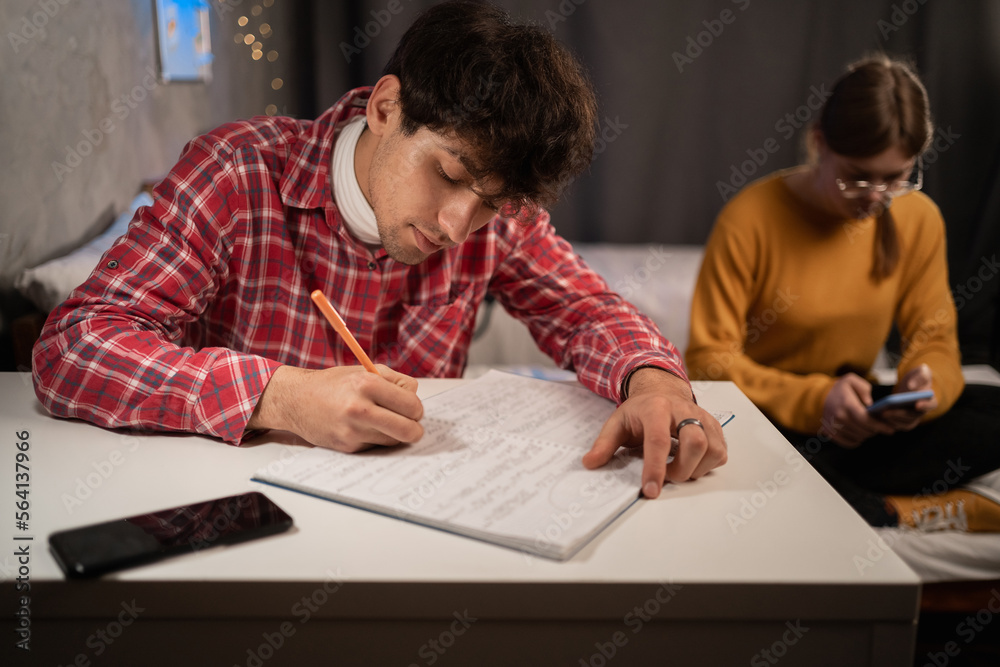 Serious college student taking notes in notebook studying in dormitory. Dorm education Serious college student taking notes in notebook studying in dormitory. Dorm education