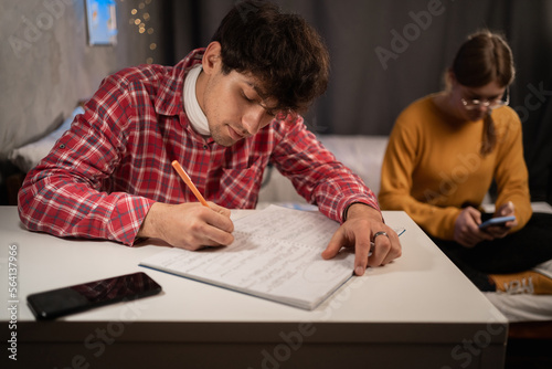 Serious college student taking notes in notebook studying in dormitory. Dorm education