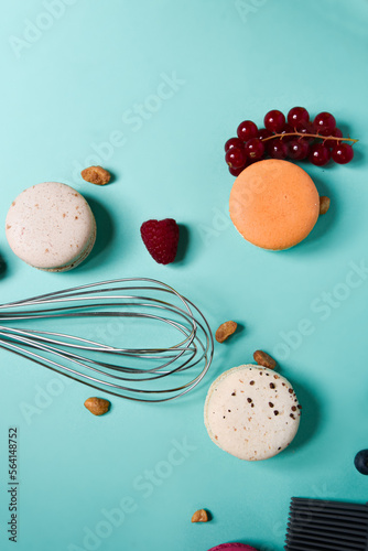 Colorful macarons. Small French cakes. Cooking, whisk, broken macarons, fruits, strawberries, raspberries and blackberries. Cooking process on a blue background, whisk, strawberries photo