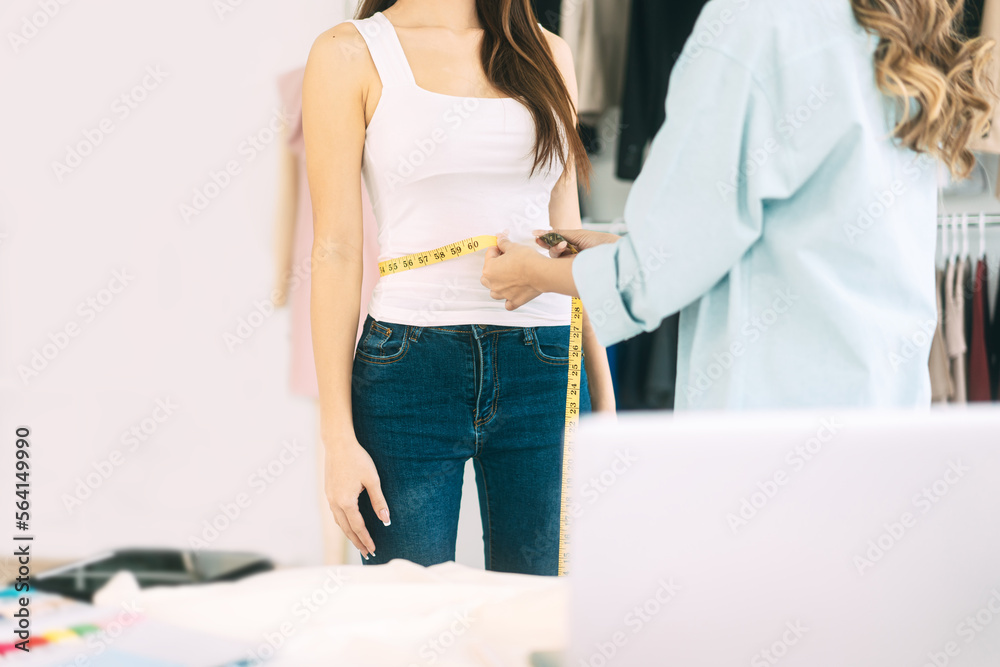 Two people tailor adult asian woman designer using tape measure for size and cutting clothes studio dressmaker