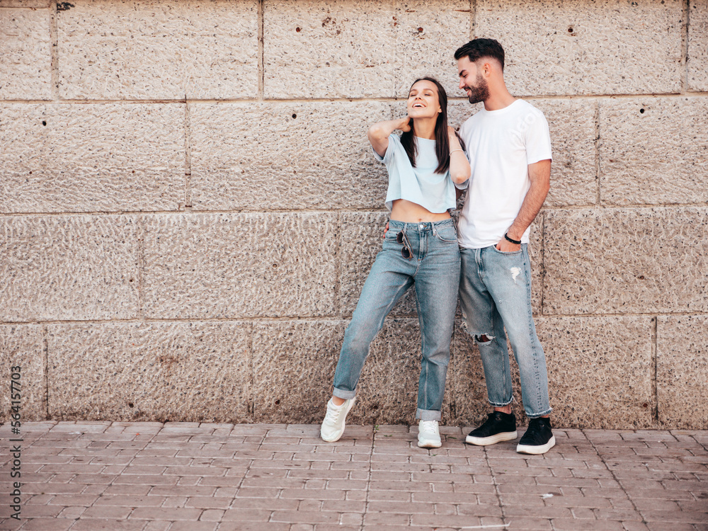 Smiling beautiful woman and her handsome boyfriend. Woman in casual summer jeans clothes. Happy cheerful family. Female having fun. Sexy couple posing in the street at sunny day. Near wall