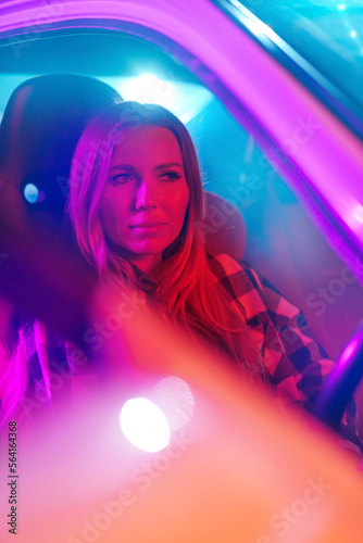 Portrait of beautiful young woman driving car at night in neon light.