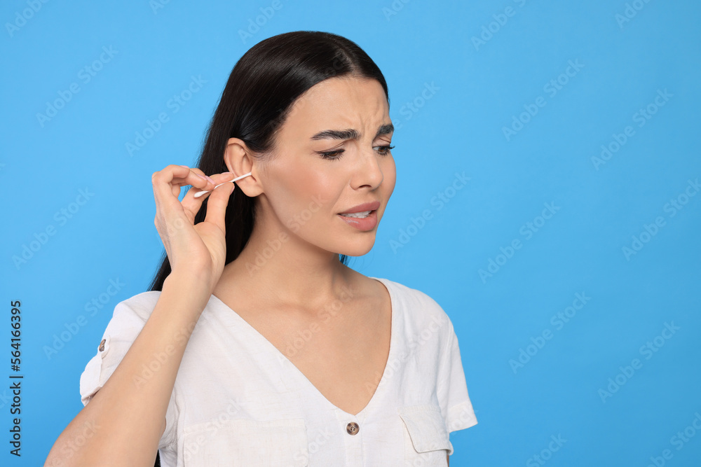 Young woman cleaning ear with cotton swab on light blue background. Space for text Young woman cleaning ear with cotton swab on light blue background. Space for text