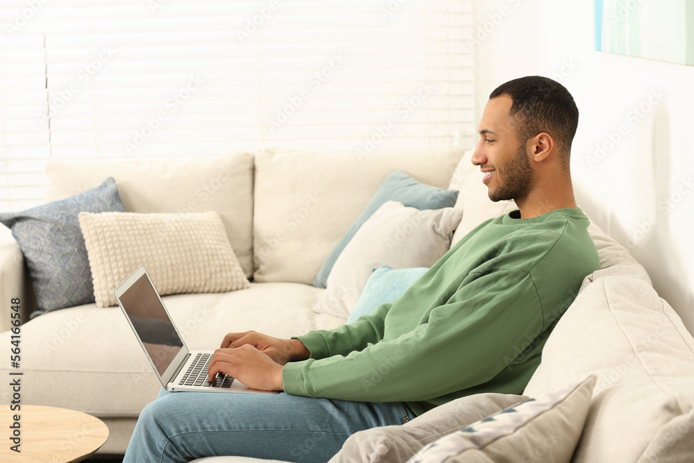 African American man typing on laptop on sofa in room