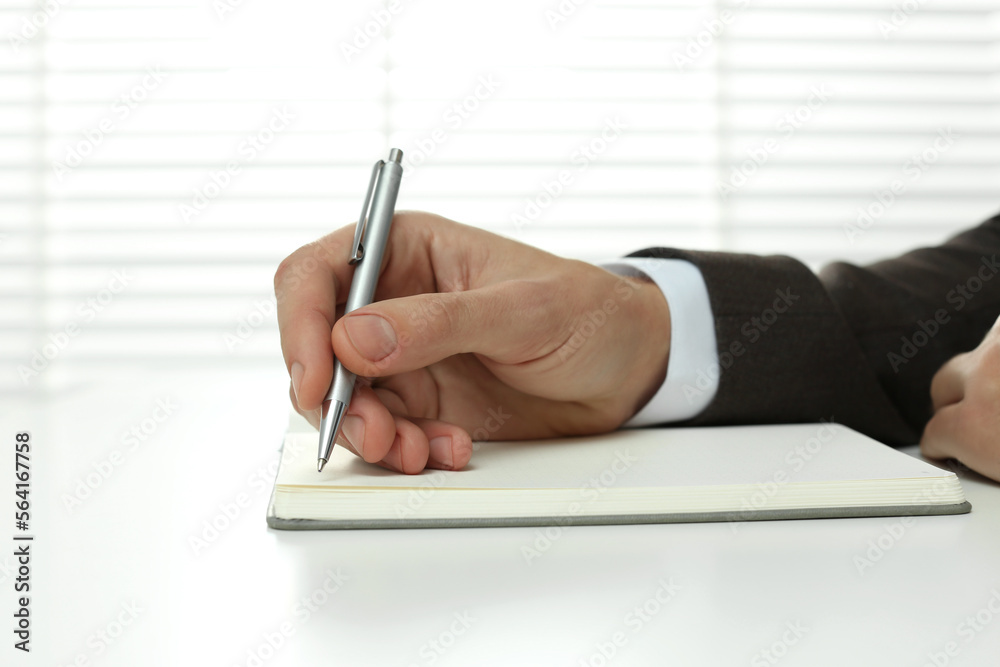 Man writing in notebook at white table indoors, closeup Man writing in notebook at white table indoors, closeup