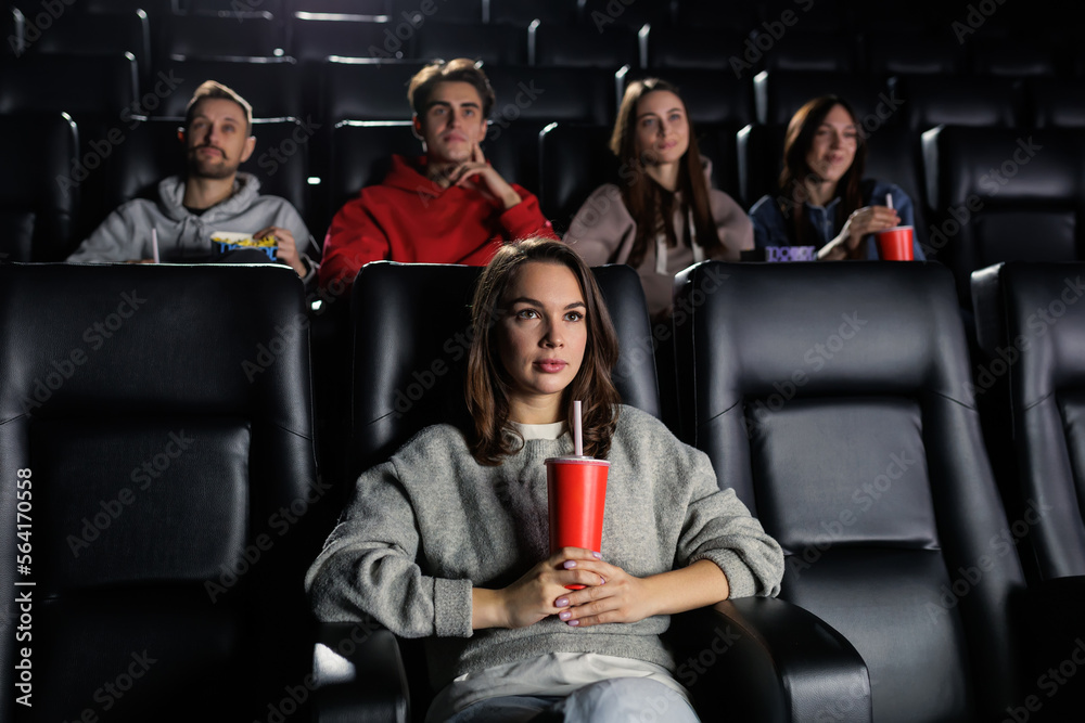 A young woman with a red cup in her hands attentively watches a movie. A woman came to the premiere at the cinema