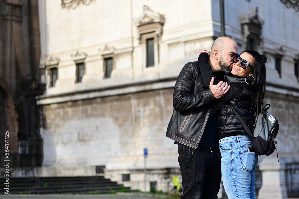Portrait of happy    smiling  Couple  in love . Casual couple portrait outdoors, tourist in Italy Happy Bearded man  kissing and hugging  Brunette woman  on the streets of  Rome neat the Roman forum